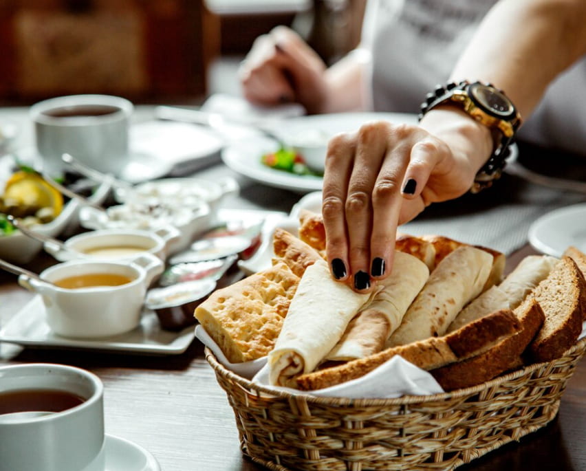 A hand reaching for bread in a basket amidst a breakfast spread