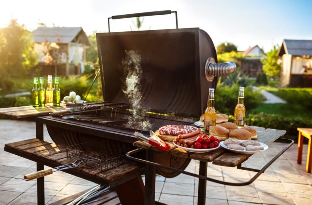 open grill with various meats, sausages, and vegetables, bottles of beer on the side