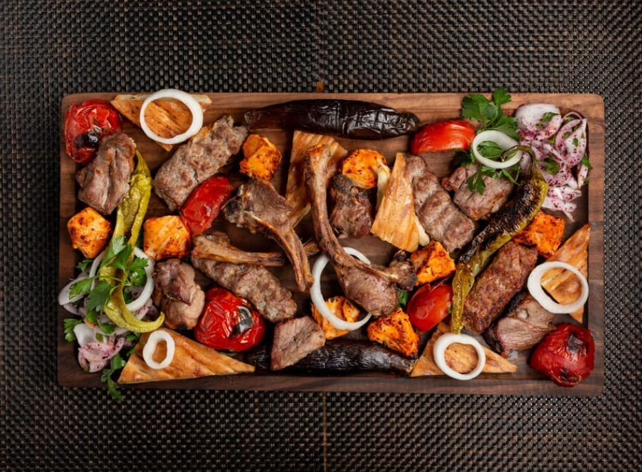 grilled ribs, lamb chops, vegetables, and onions, garnished with fresh herbs on a tablecloth