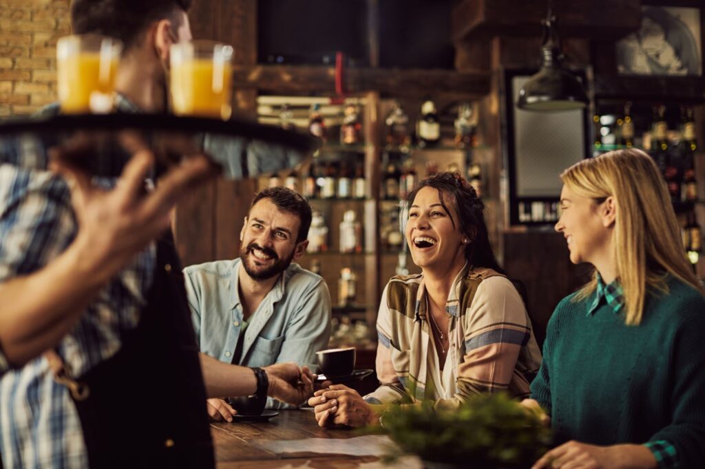 Cheerful friends having fun while waiter bring them drinks